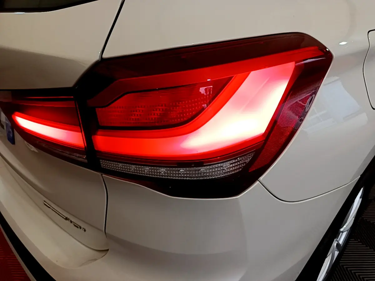 Gros plan sur le feu arrière droit rouge d’un BMW X1 sDrive18i blanc, avec partie de la carrosserie visible.