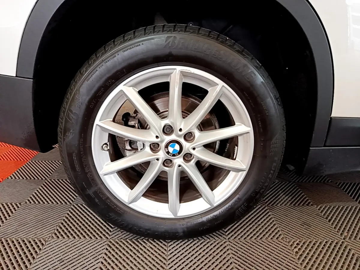 Gros plan sur la roue avant droite blanche d'un BMW X1 sDrive18i Lounge avec jante alliage à 10 branches.