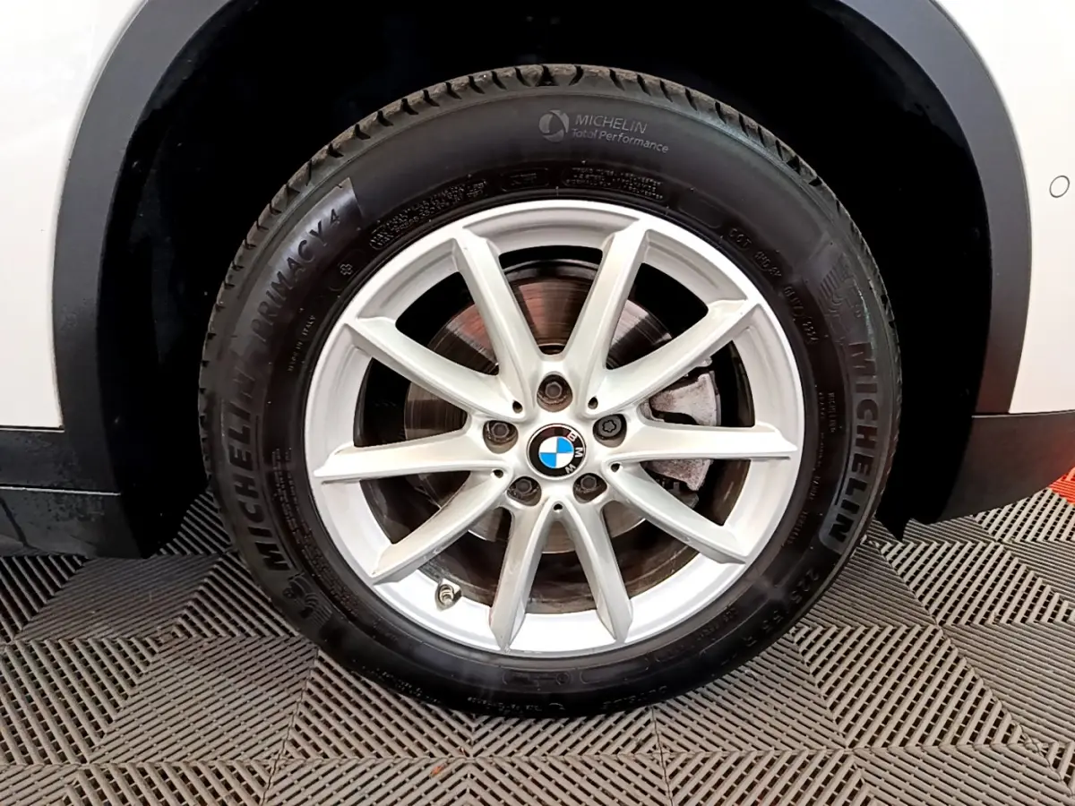 Gros plan sur la roue avant droite blanche d’un BMW X1 sDrive18i Lounge avec jante alliage et pneu Michelin.