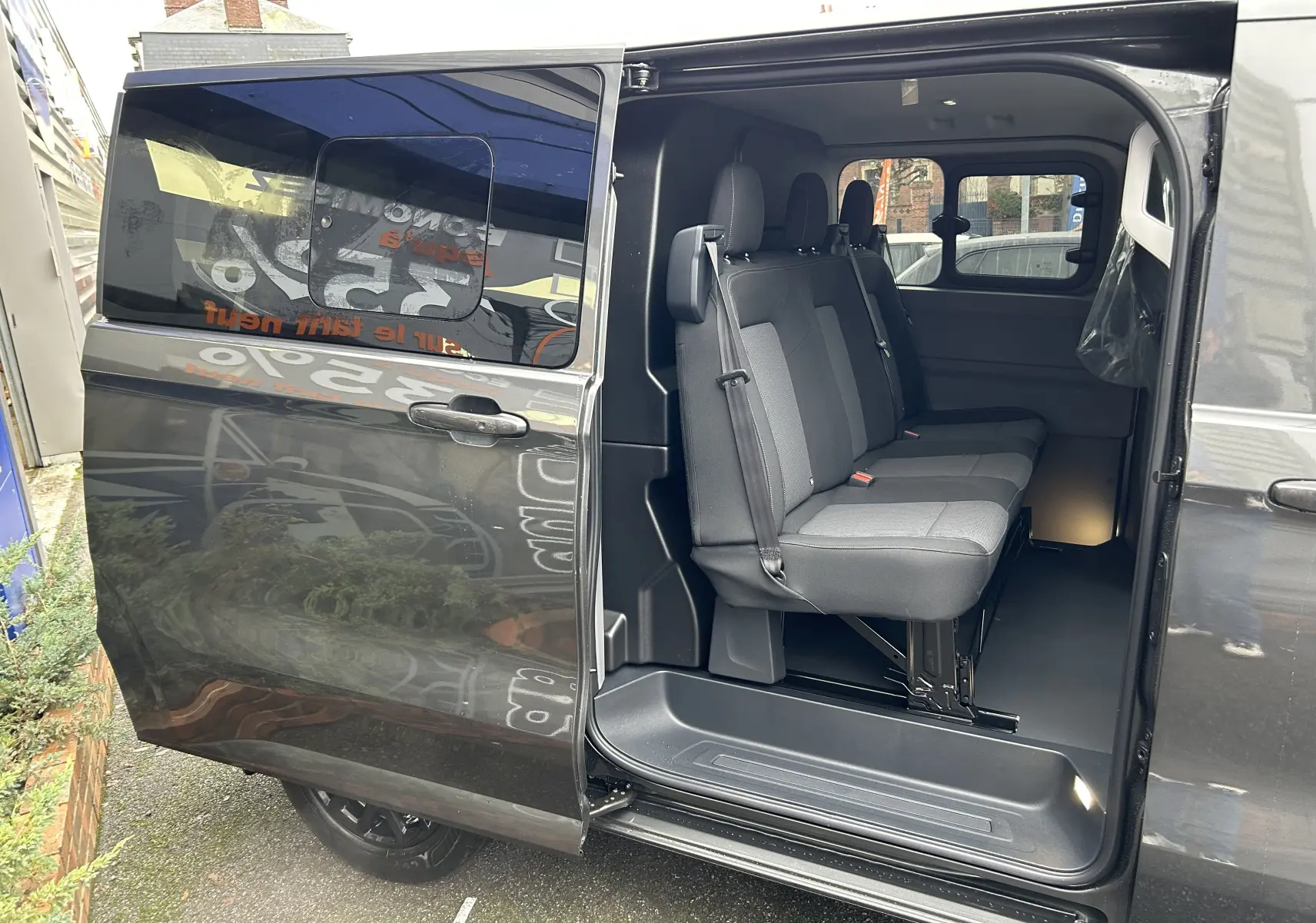 Vue latérale gauche du Volkswagen Transporter T7 ProCab graphite Dust avec porte coulissante ouverte et sièges arrière en tissu visibles.