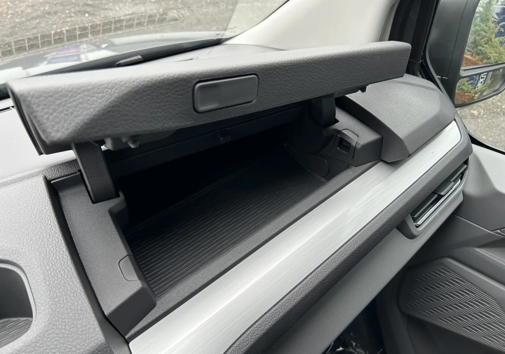 Vue intérieure du Volkswagen Transporter T7 ProCab 2026 montrant la boîte à gants ouverte côté passager avec finition gris clair.