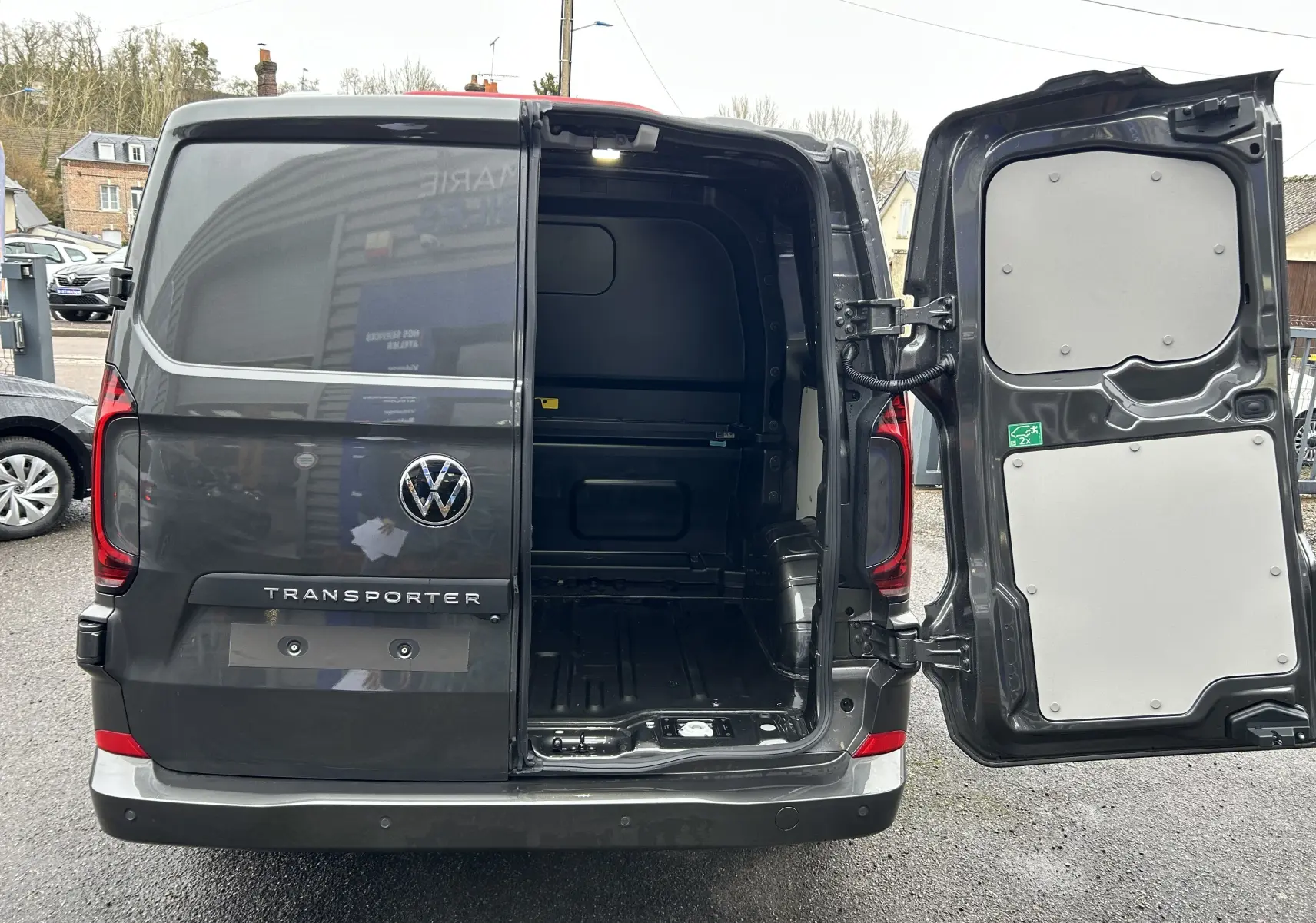 Vue arrière d’un Volkswagen Transporter T7 ProCab graphite Dust avec porte droite ouverte montrant l’espace de chargement vide.