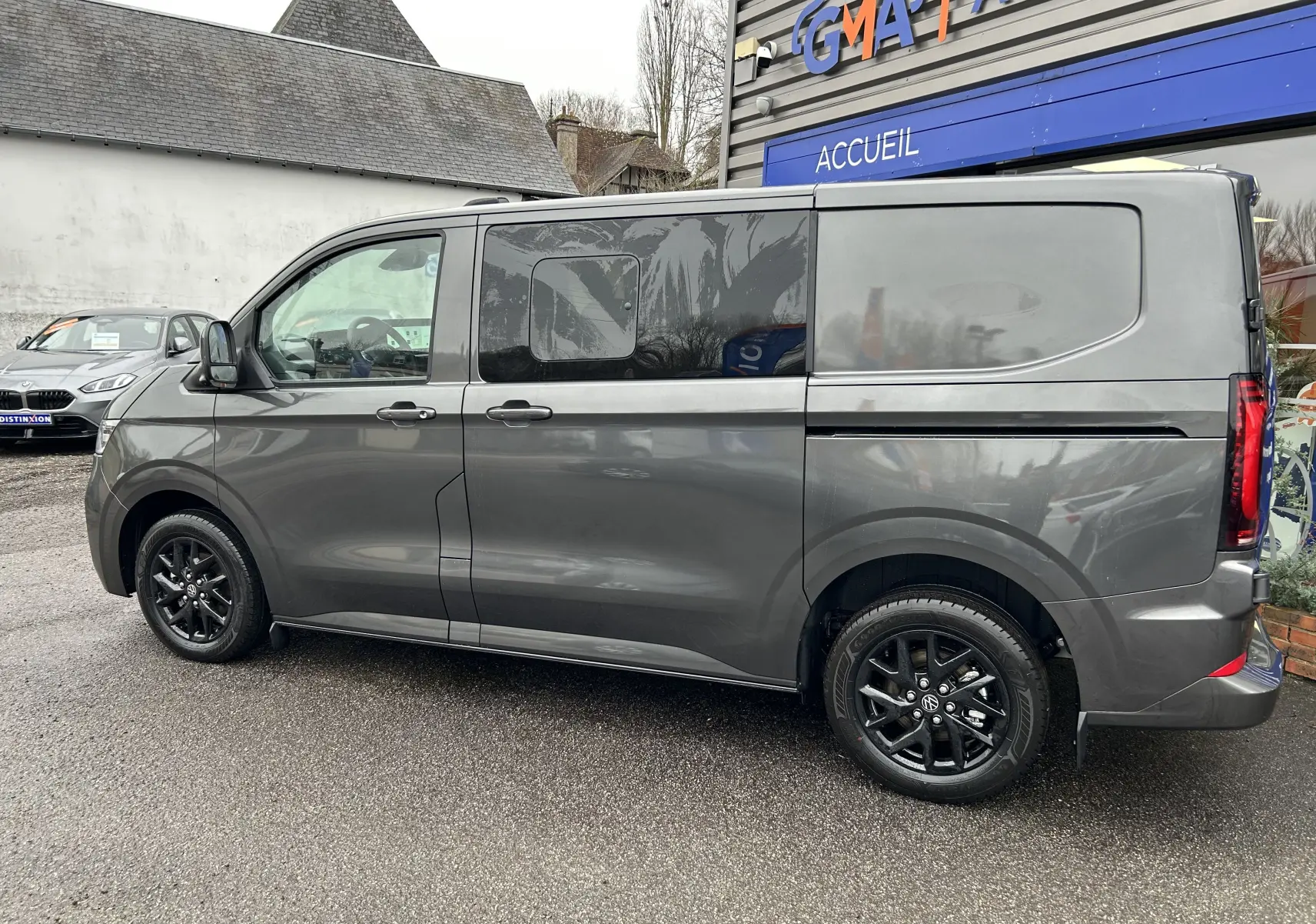 Vue de profil côté gauche d’un Volkswagen Transporter T7 ProCab graphite avec jantes noires brillantes et porte latérale coulissante.