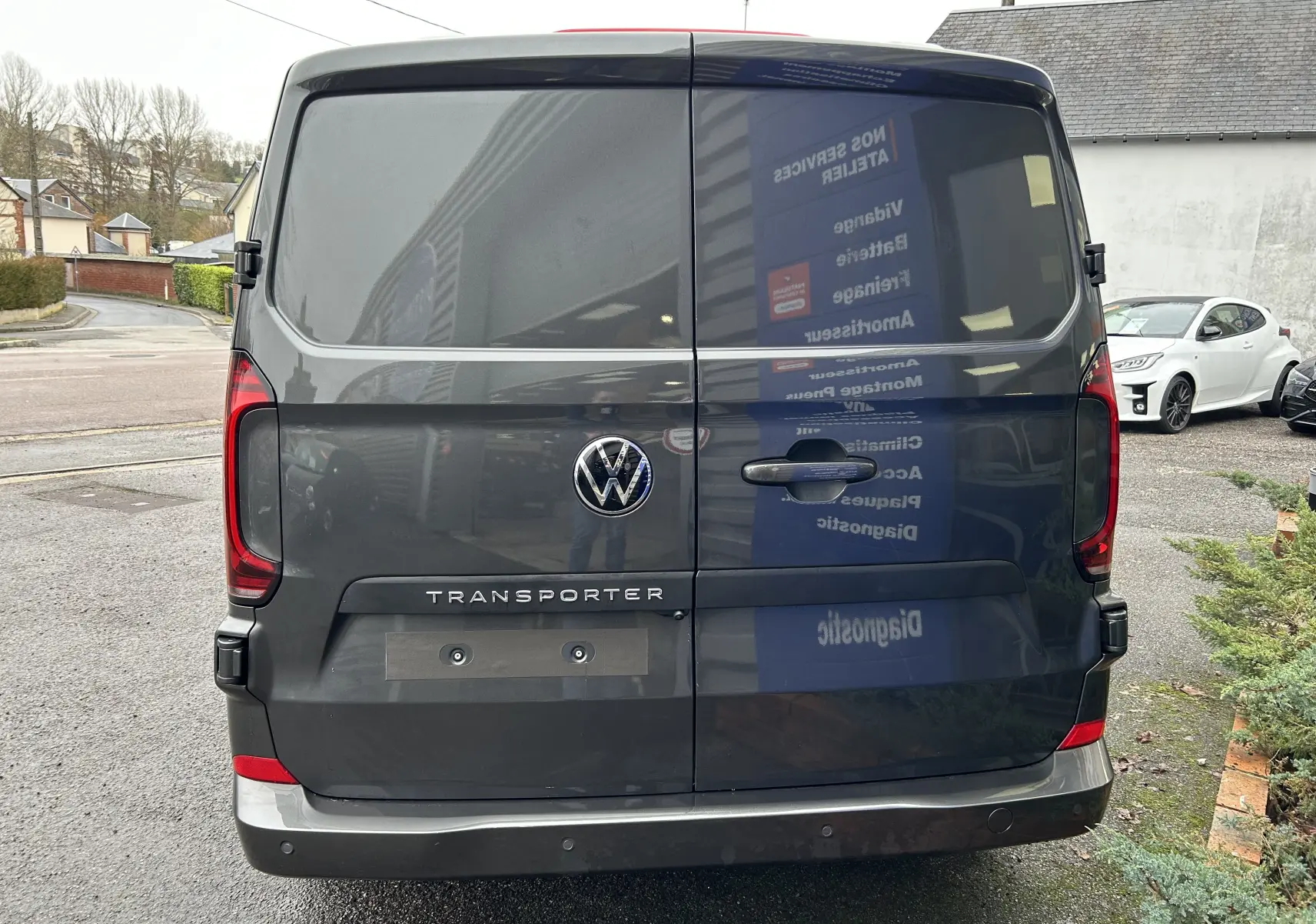 Vue arrière d'un Volkswagen Transporter T7 ProCab graphite dust avec logo VW et feux arrière rouges.
