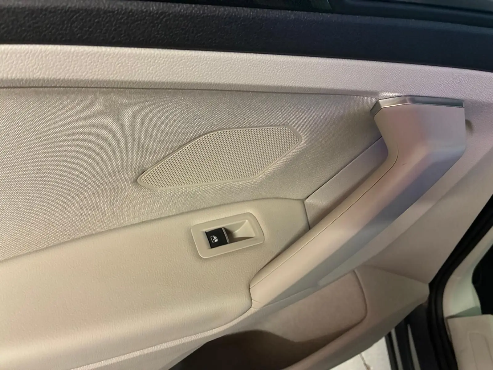Gros plan sur la poignée intérieure côté gauche du Volkswagen Tiguan gris, avec bouton de commande de vitre électrique.