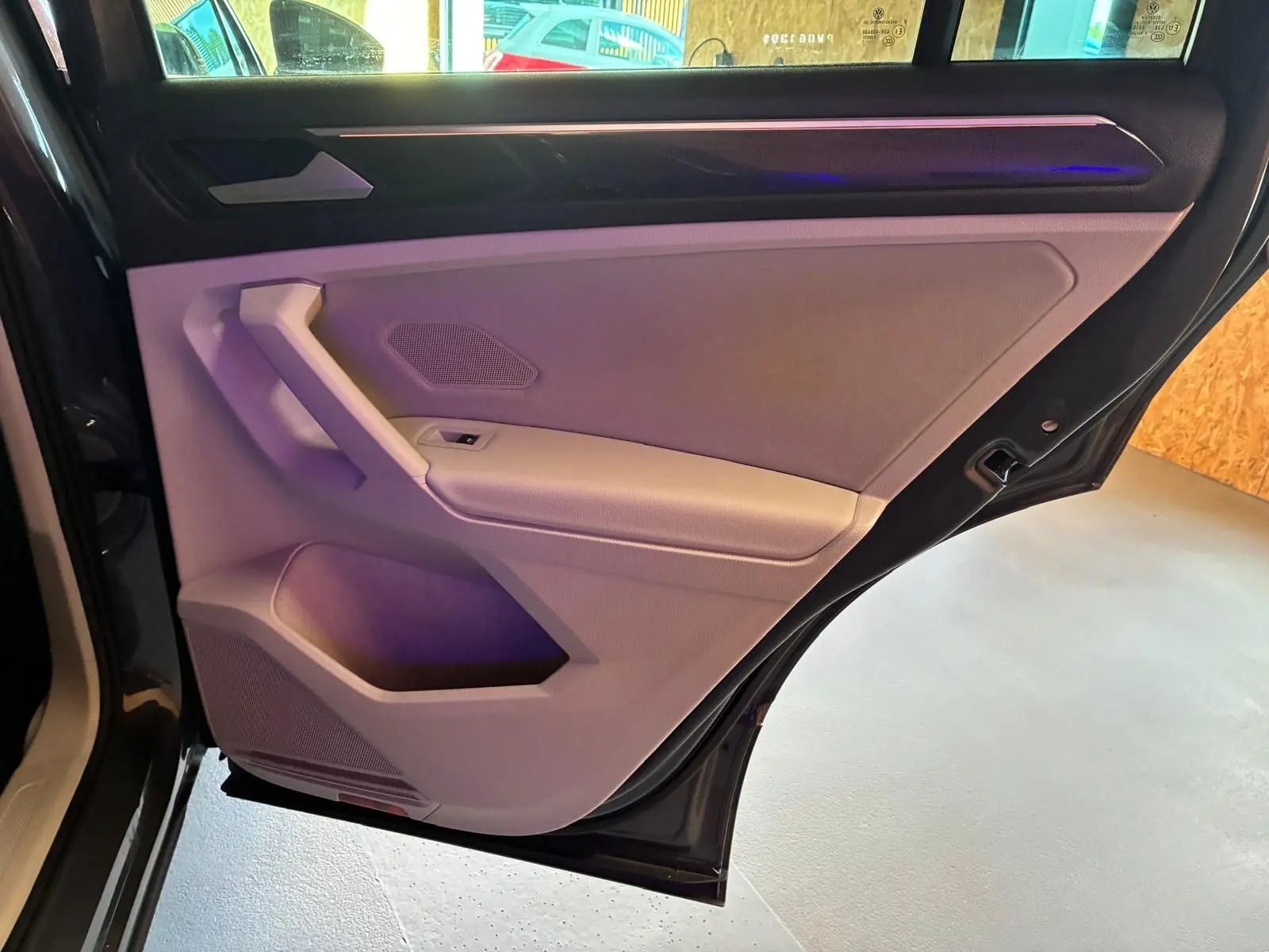 Vue intérieure du panneau de porte arrière gauche gris clair du Volkswagen Tiguan 2023 avec éclairage d'ambiance violet.