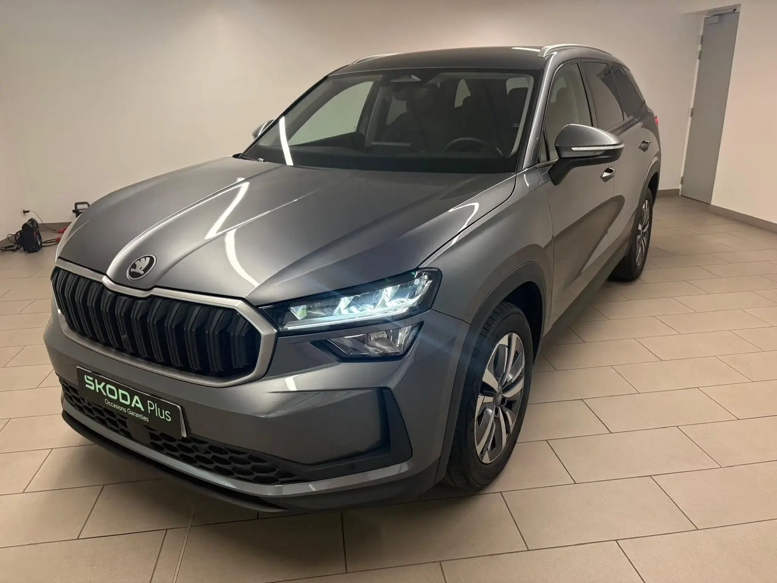 Vue 3/4 avant droit du Skoda Kodiaq 2025 gris graphite avec calandre noire et phares allumés en intérieur.