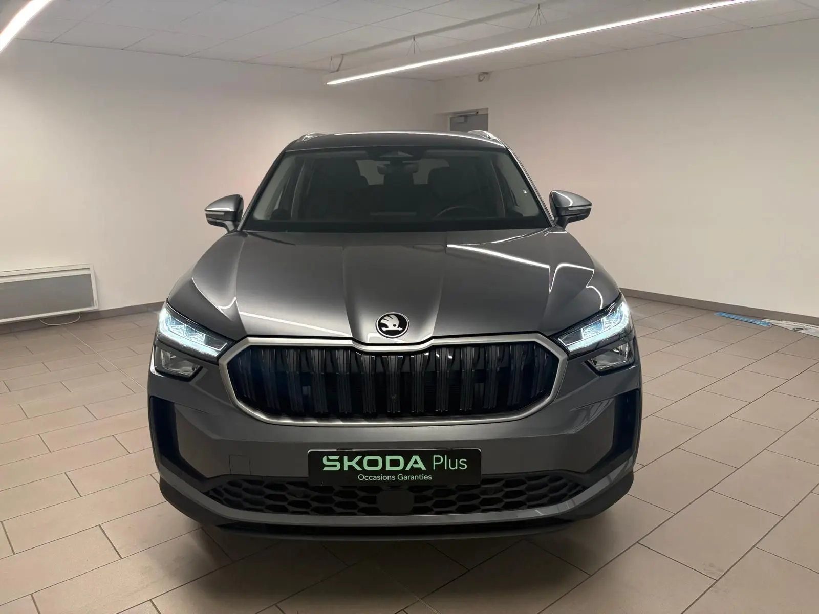 Vue frontale d'un Skoda Kodiaq gris graphite 2025 avec calandre noire et phares LED allumés en intérieur.