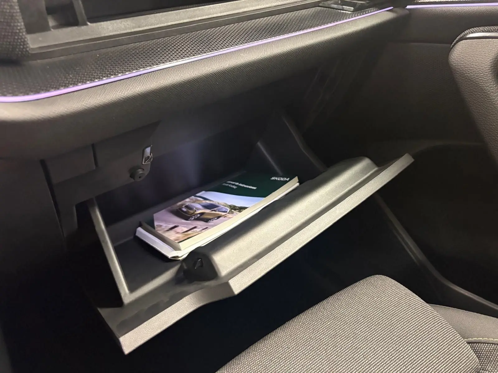 Gant de boîte ouvert côté passager du Skoda Kodiaq gris graphite 2025, avec manuel utilisateur visible à l'intérieur.