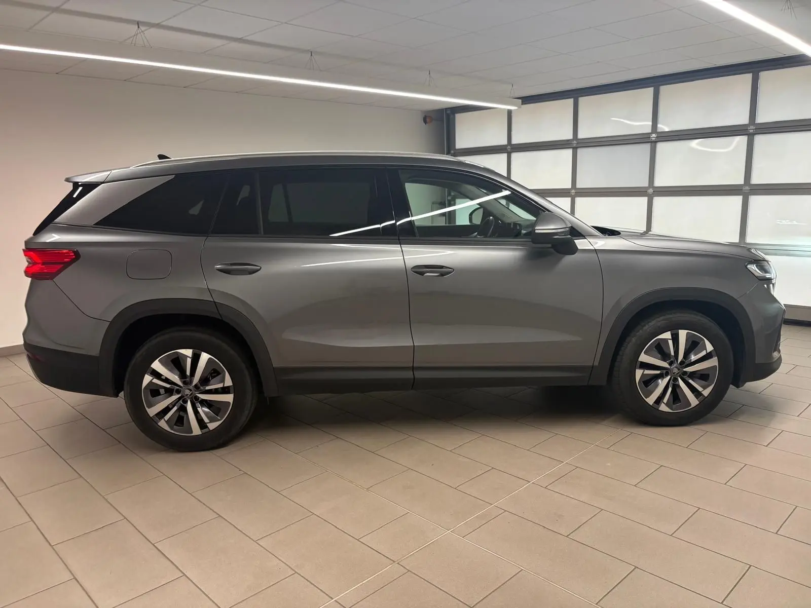 Vue de profil côté gauche d'un Skoda Kodiaq 2025 gris graphite avec jantes alliage et toit noir en intérieur.
