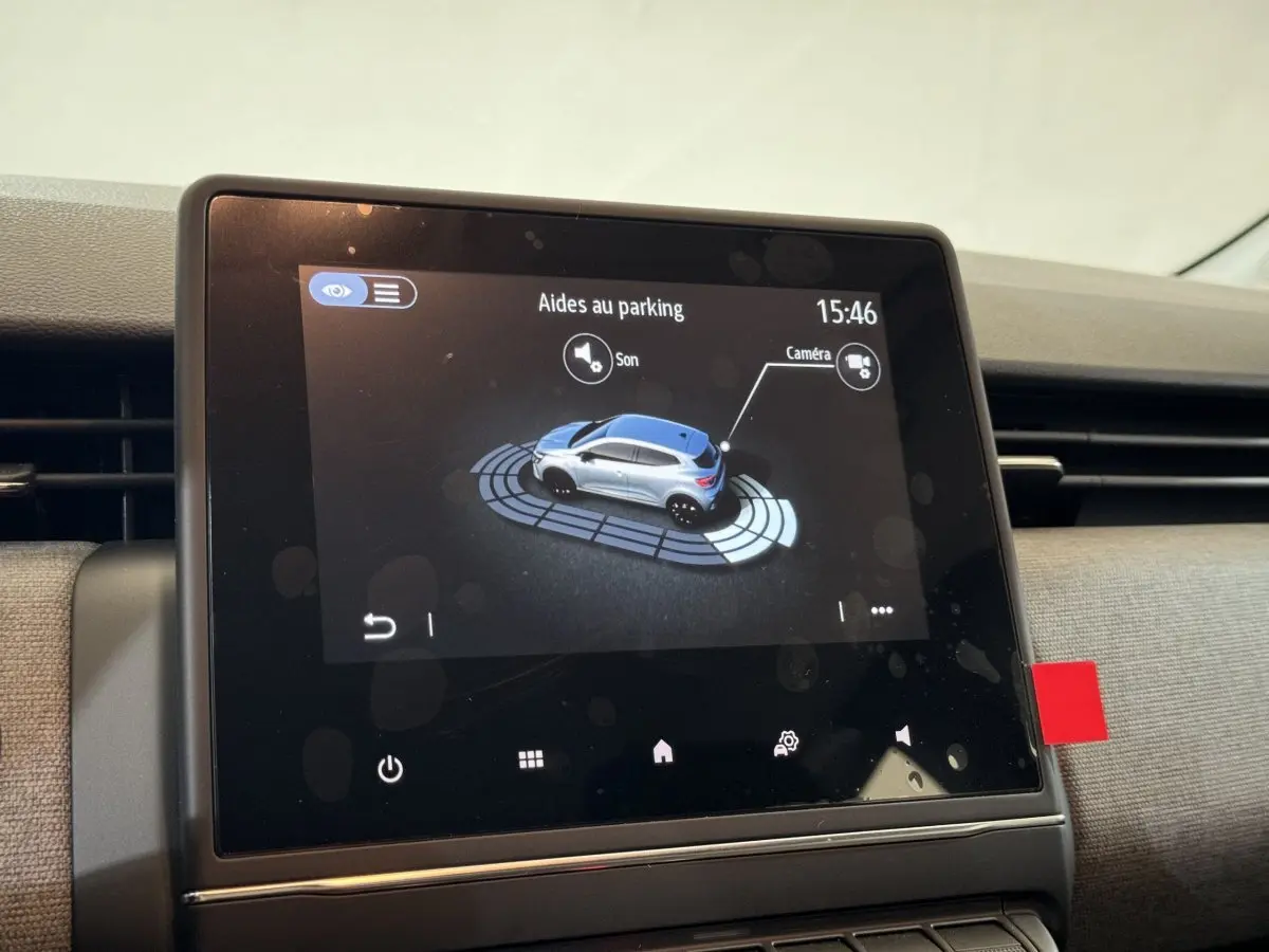 Écran tactile central montrant l'aide au parking d'une Renault Clio gris clair vue de profil sur l'affichage numérique.