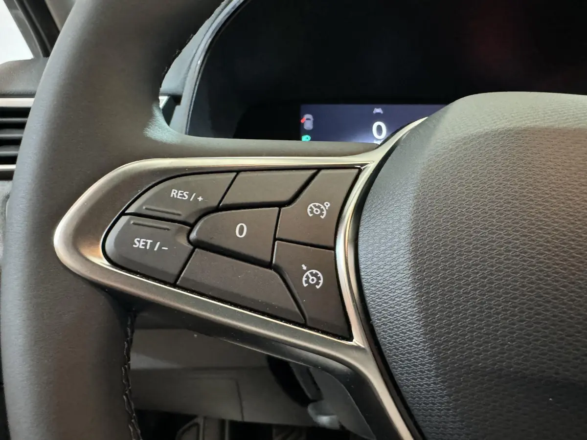 Gros plan sur les commandes du régulateur de vitesse au volant cuir noir de la Renault Clio gris clair 2025 Evolution Blue dCi 100