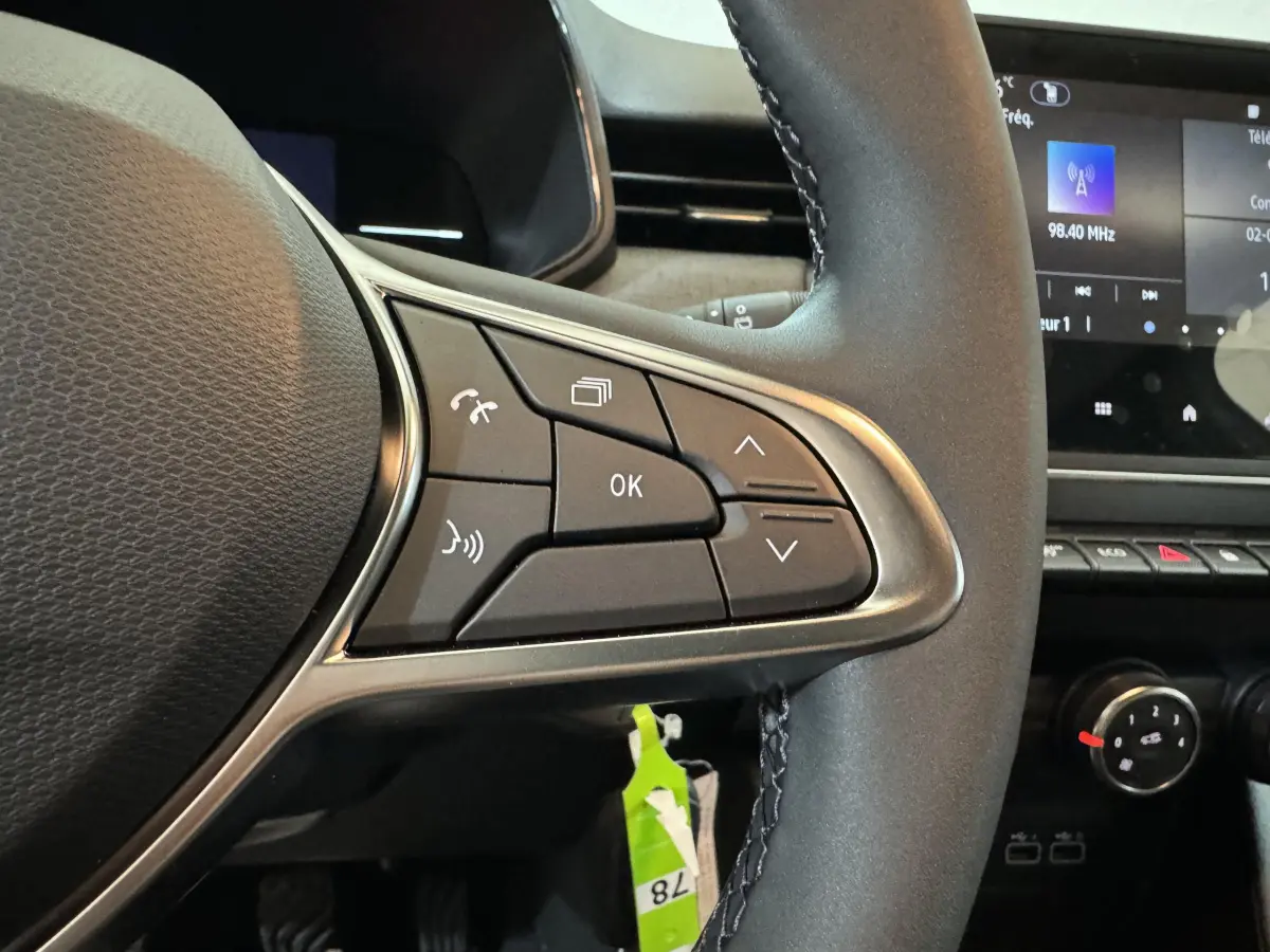 Gros plan sur les commandes au volant cuir noir de la Renault Clio gris clair, avec écran tactile en arrière-plan.