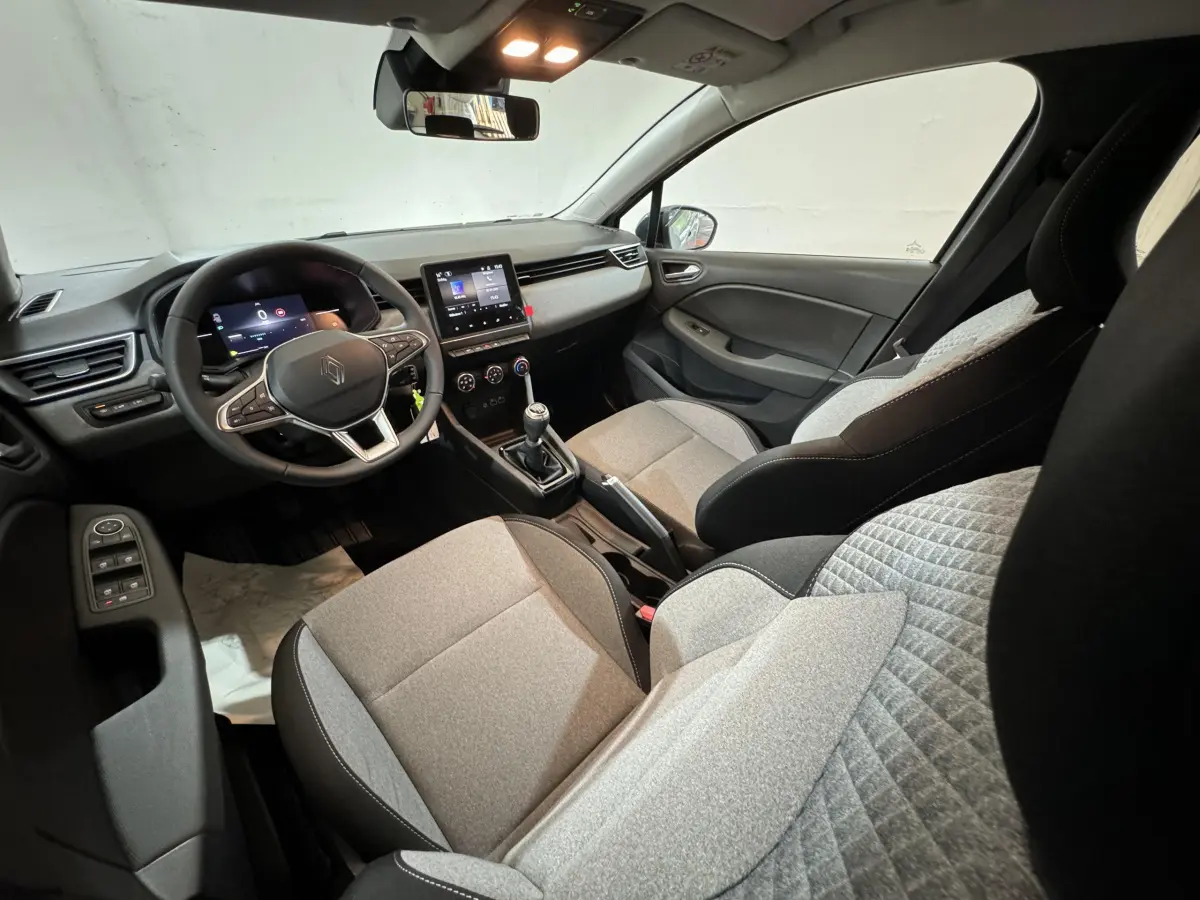 Intérieur de Renault Clio 2025 vu côté conducteur, sièges gris clair et tableau de bord avec écran tactile central.