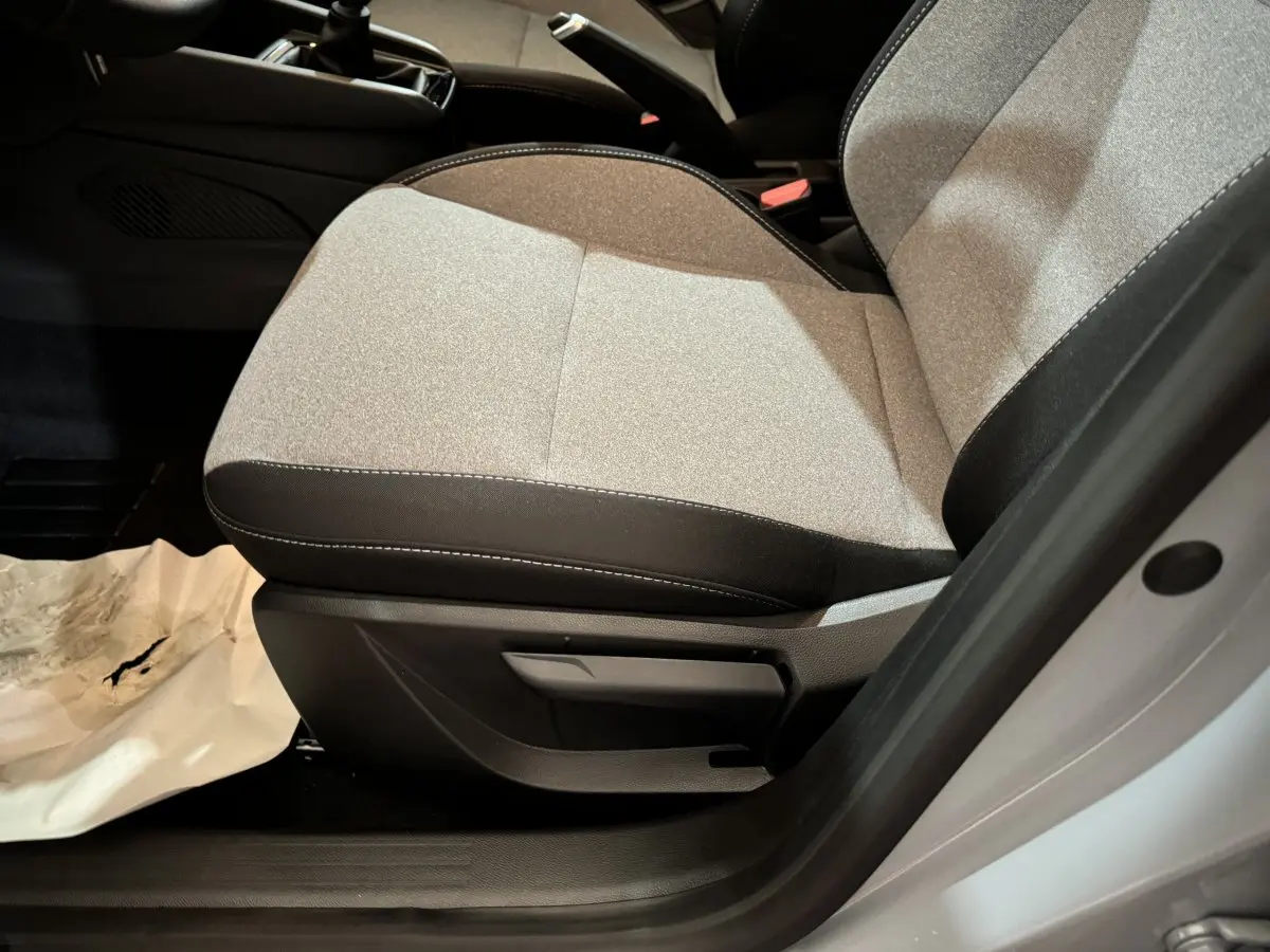 Gros plan sur le siège avant droit gris clair de la Renault Clio Evolution Blue dCi 100 2025 avec volant et console partiellement visibles.