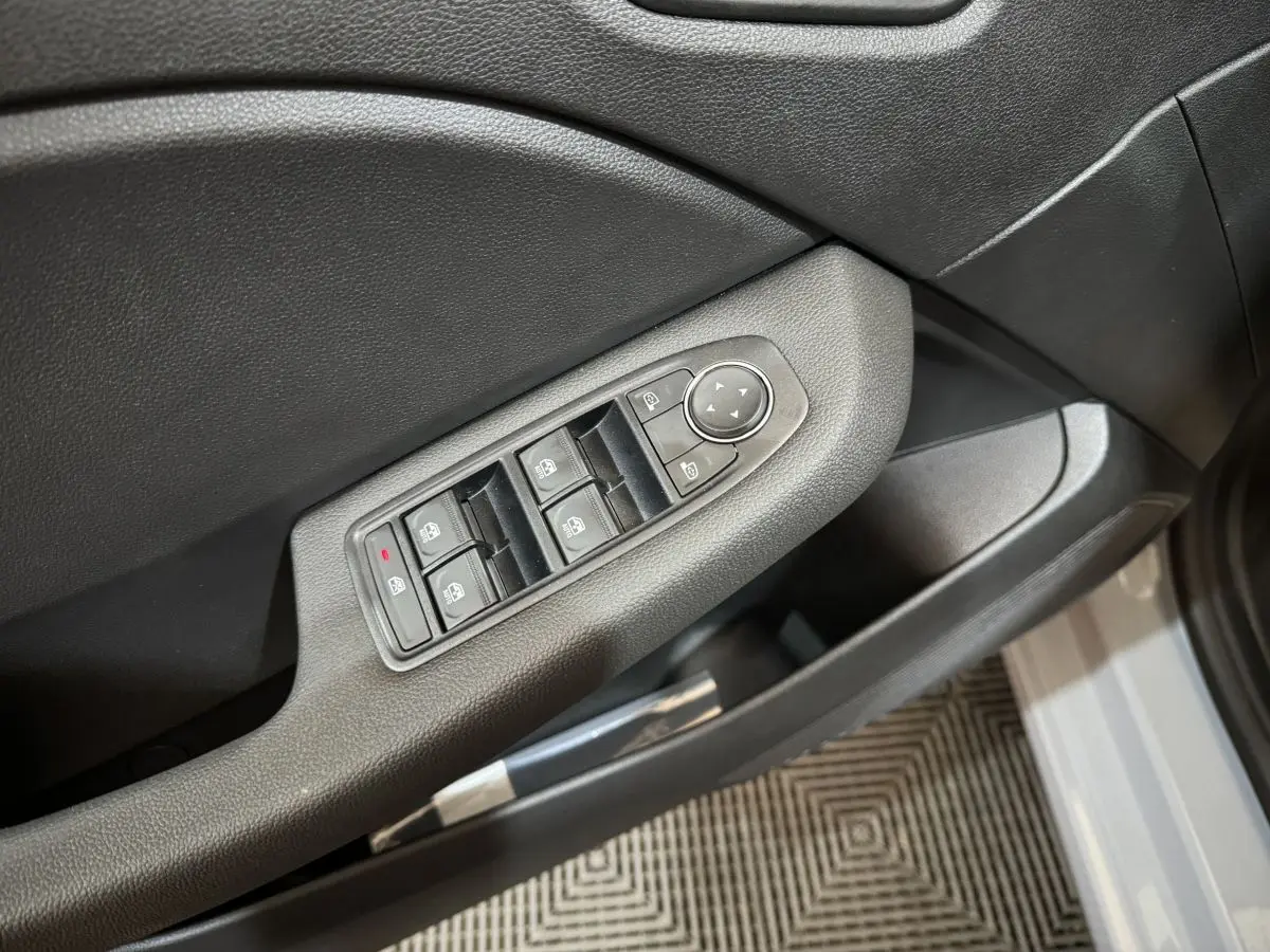 Gros plan sur la commande des vitres électriques côté conducteur d'une Renault Clio gris clair, porte ouverte.