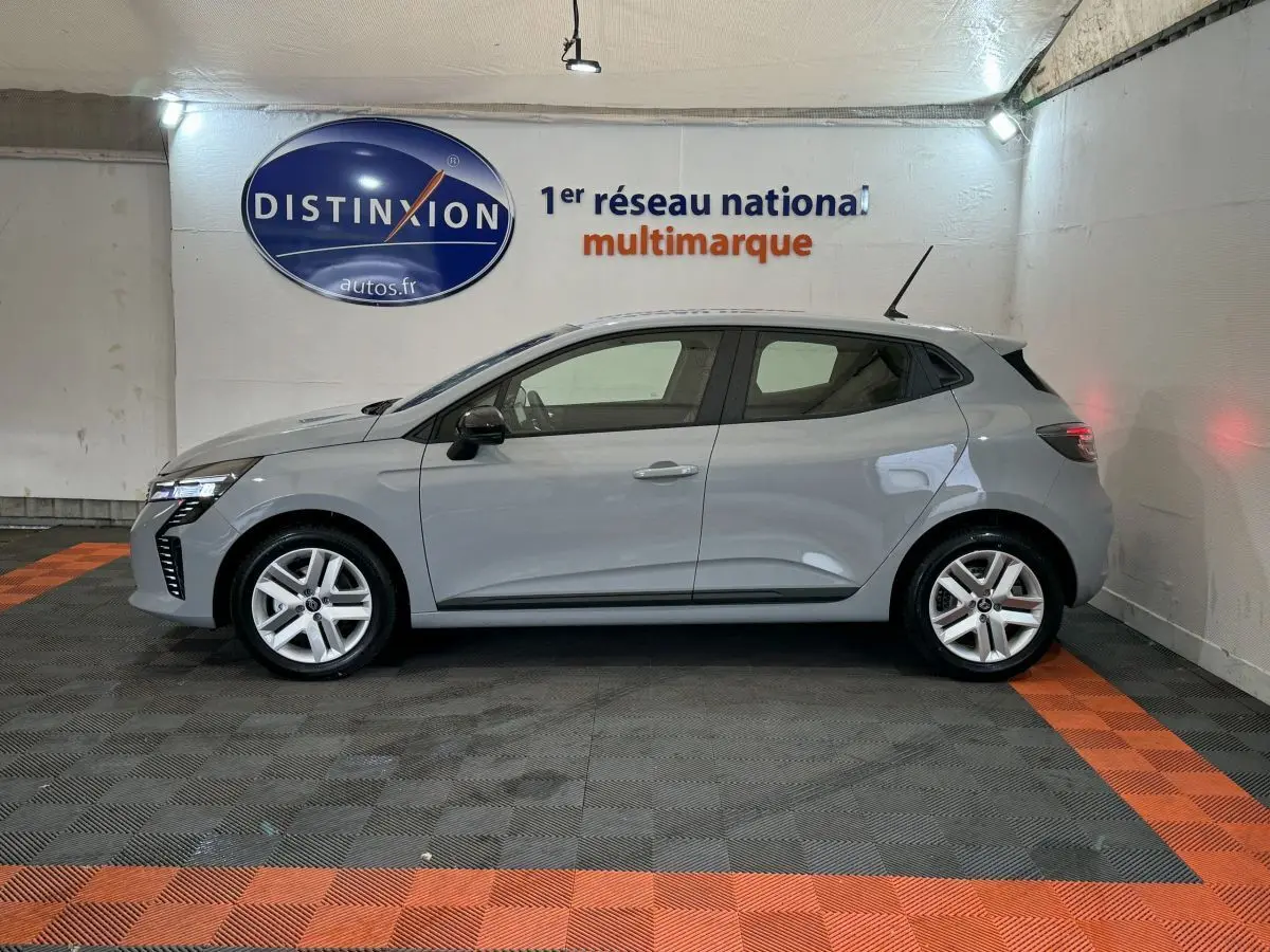 Profil côté gauche d'une Renault Clio gris clair 2025 garée en intérieur avec éclairage neutre et jantes alliage.