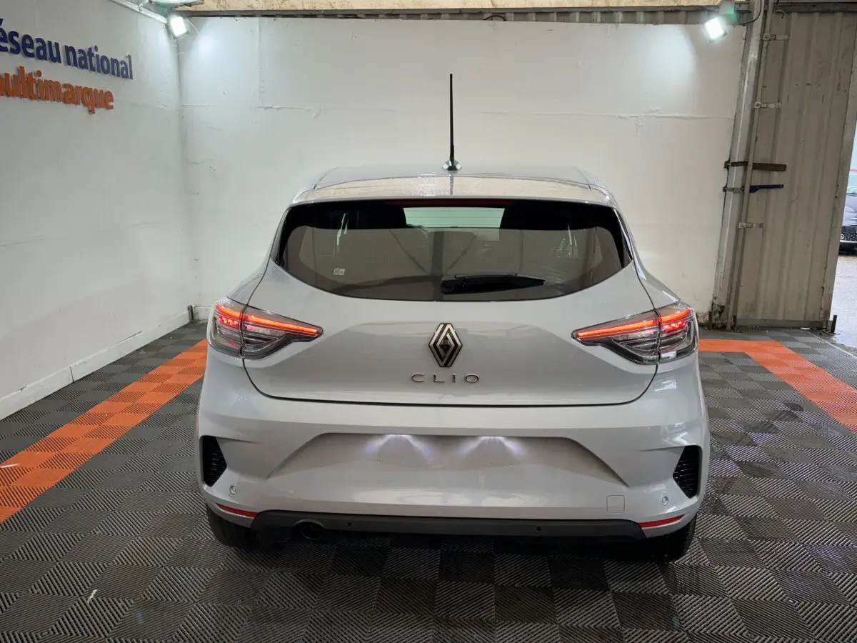 Vue arrière d'une Renault Clio gris clair 2025 avec feux LED allumés dans un garage éclairé