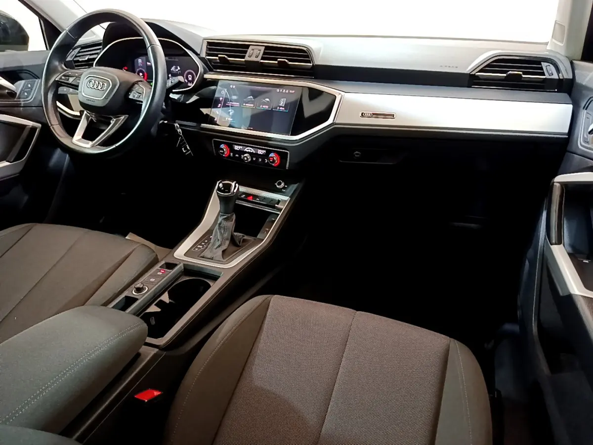 Vue intérieure côté conducteur de l'Audi Q3 35 TDI 2021, tableau de bord moderne avec écran tactile et volant cuir noir.