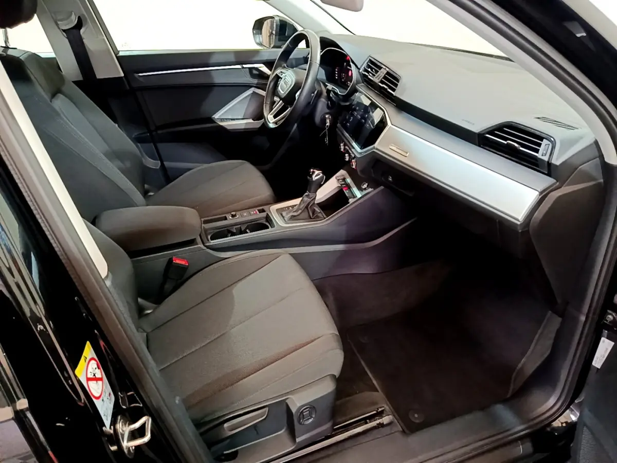 Intérieur avant droit de l’Audi Q3 noir 2021, montrant sièges tissu, tableau de bord moderne et volant multifonctions cuir.