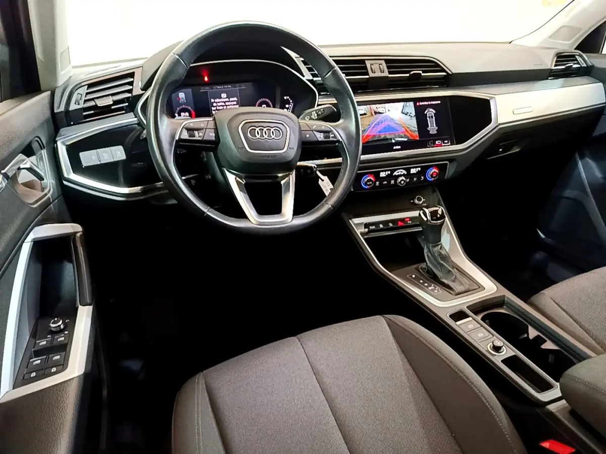 Vue intérieure avant de l'Audi Q3 35 TDI 150 S tronic, tableau de bord noir avec écran tactile et volant cuir multifonctions.