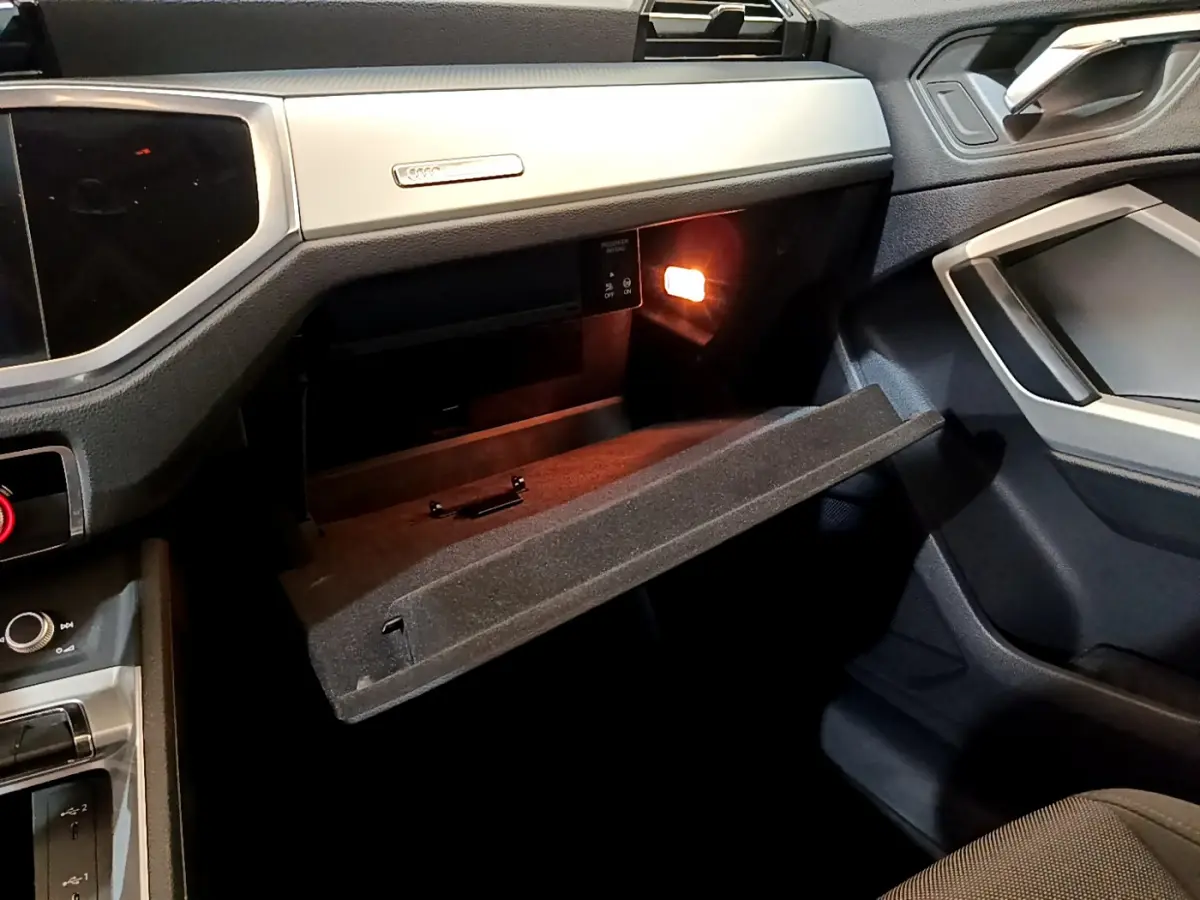 Vue intérieure côté passager de l'Audi Q3 noir 35 TDI 2021 avec boîte à gants ouverte et éclairage intérieur allumé.