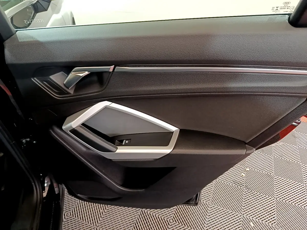 Vue intérieure du panneau de porte côté gauche de l'Audi Q3 noir, avec poignée argentée et commande de vitre.