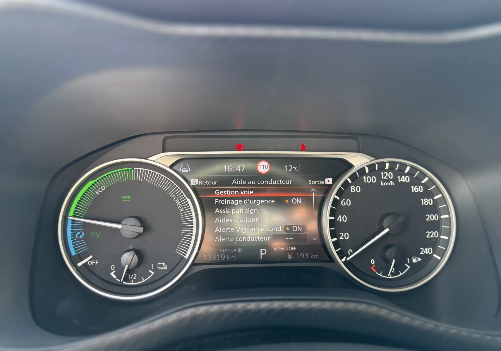 Vue rapprochée du tableau de bord du Nissan Juke Hybrid gris, affichant les compteurs et l'écran d'aide au conducteur.