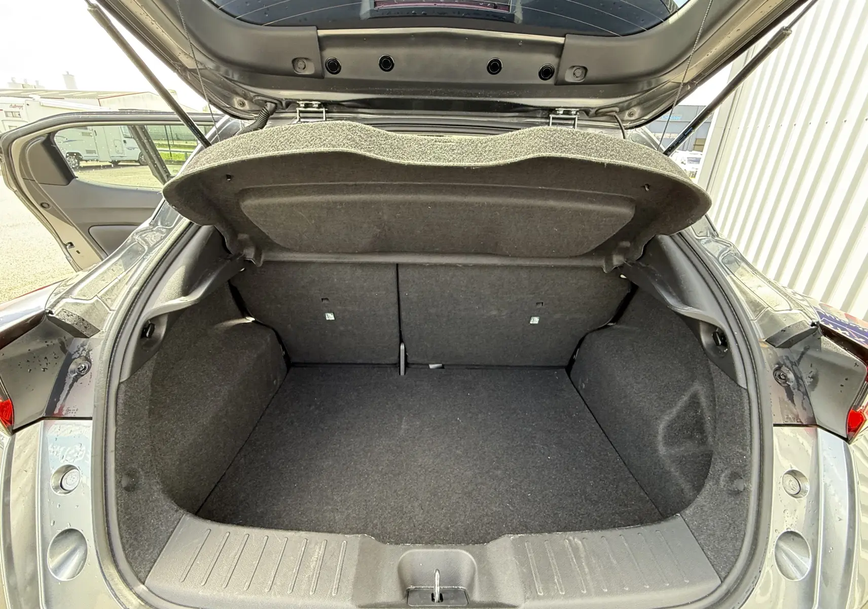 Coffre ouvert vu de l'arrière d'un Nissan Juke gris squale métal, montrant l'espace de chargement vide et la trappe de coffre relevée.