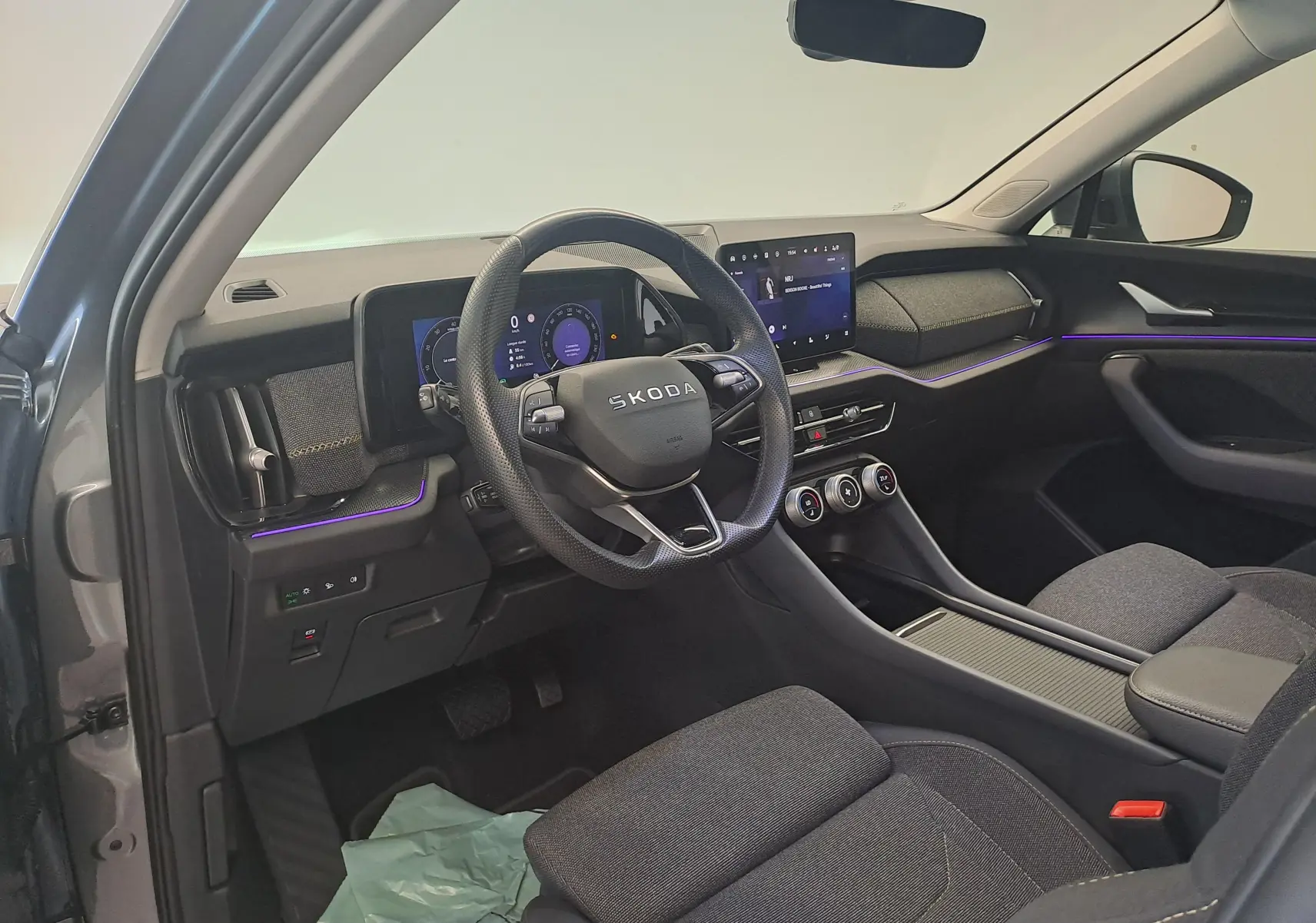 Vue intérieure côté conducteur du Skoda Kodiaq gris graphite 2025, avec tableau de bord numérique et éclairage d'ambiance violet.