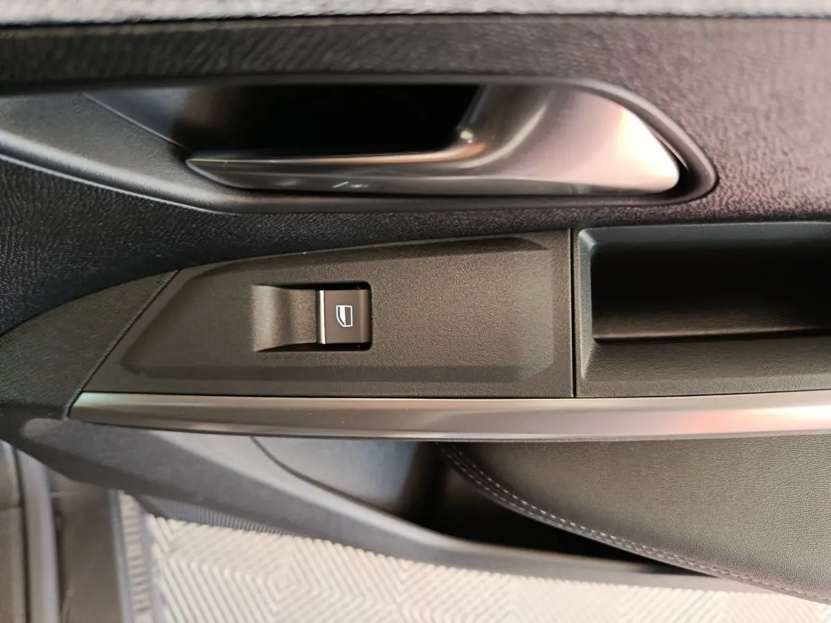 Détail de la poignée intérieure et bouton de lève-vitre côté gauche d'un Peugeot 3008 gris foncé 2025.