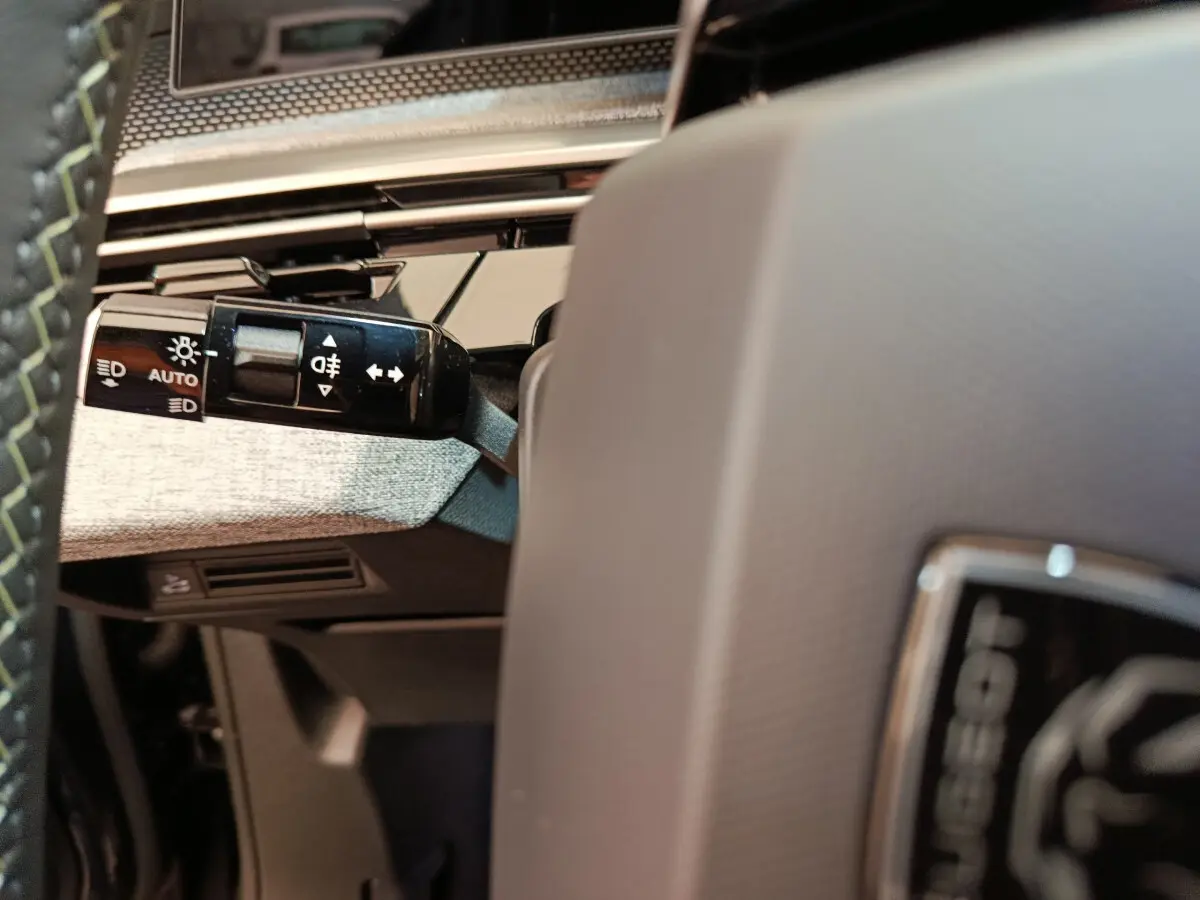 Détail du commodo d'éclairage à gauche du volant gris clair dans l'habitacle du Peugeot 3008 gris foncé 2025.