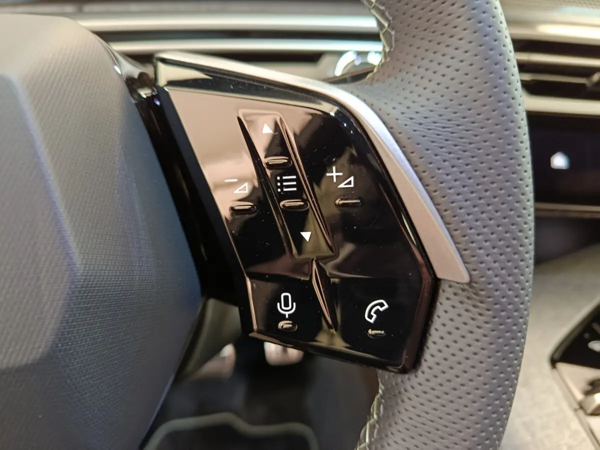 Gros plan sur les commandes tactiles noires du volant cuir perforé du Peugeot 3008 gris foncé, version hybride 2025.