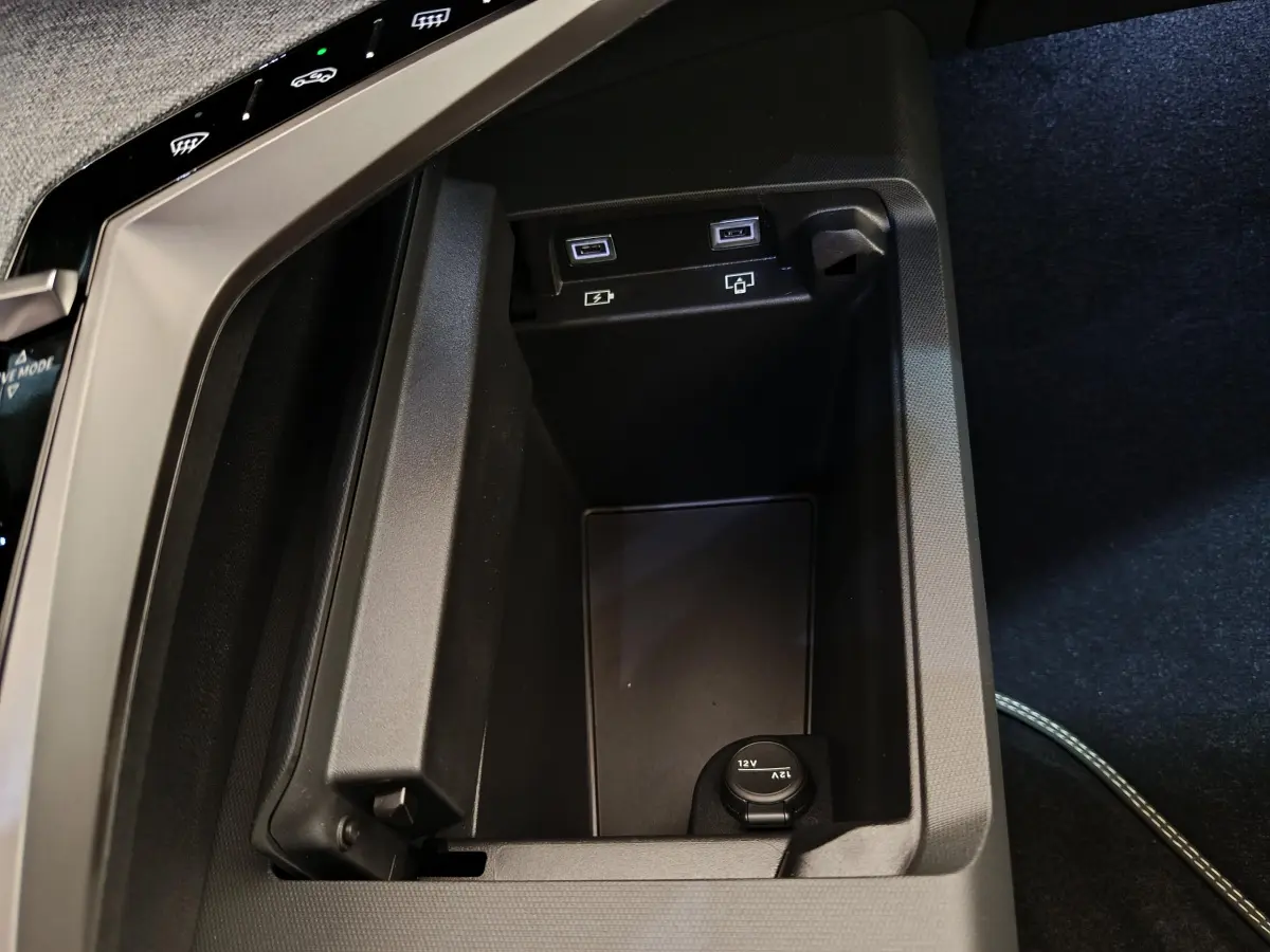 Gros plan sur la console centrale noire du Peugeot 3008 hybride 2025, avec prises USB et prise 12V visibles.