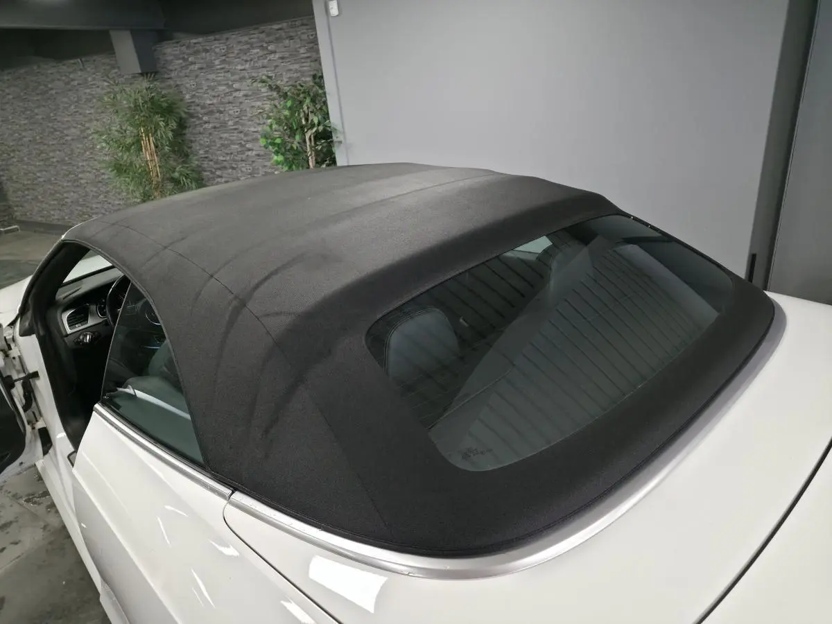 Vue arrière côté gauche d'un Audi A5 Cabriolet blanc avec capote noire fermée dans un garage.