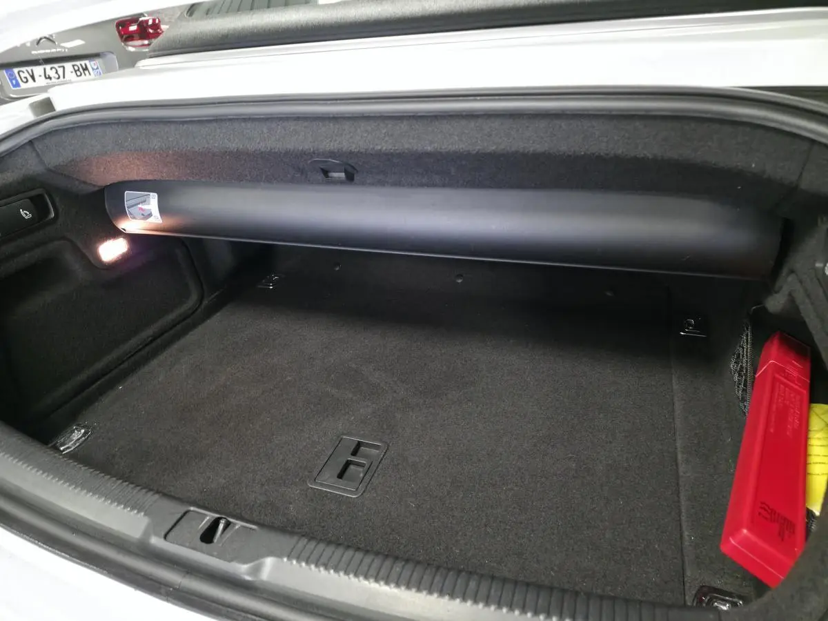 Coffre ouvert d'une Audi A5 Cabriolet blanc, montrant un intérieur noir propre avec un triangle de signalisation rouge.