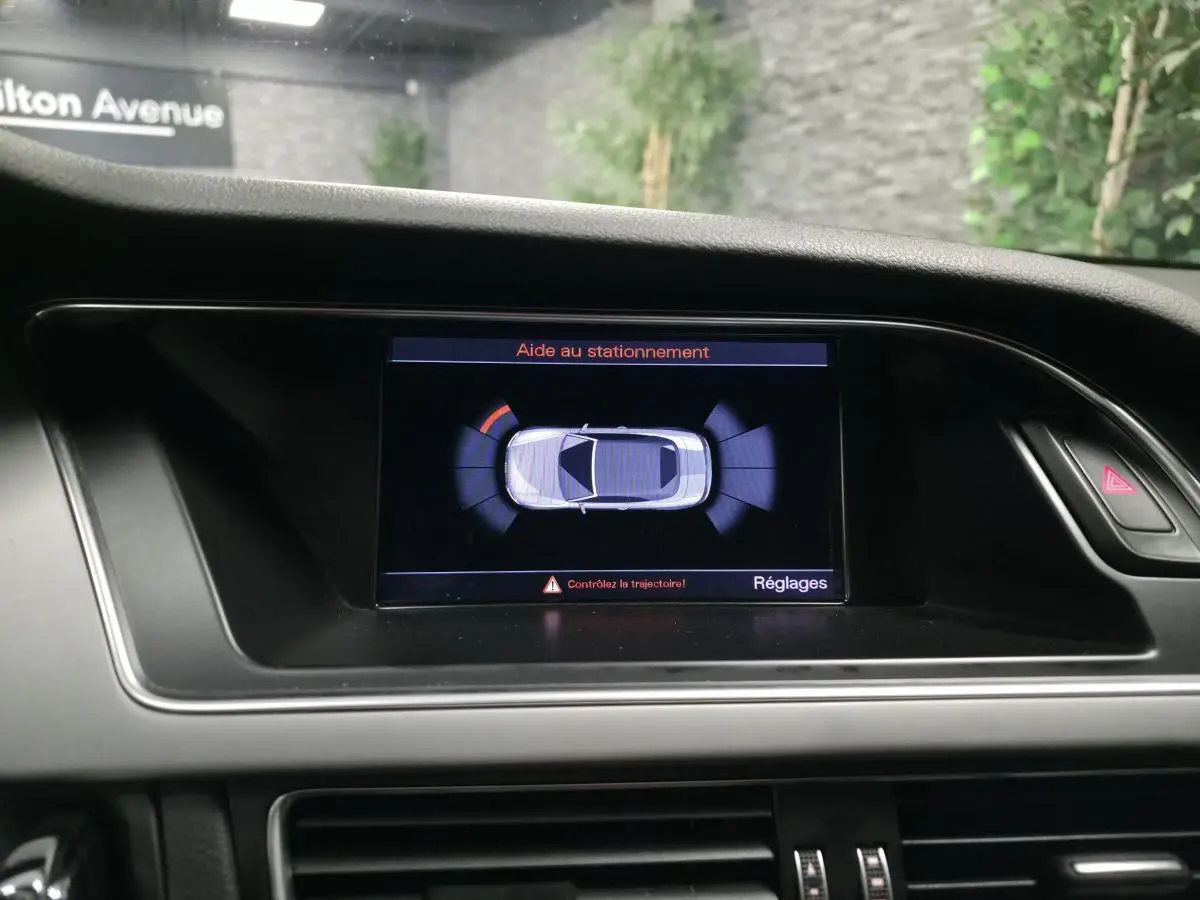 Écran central de l'Audi A5 Cabriolet blanc affichant l'aide au stationnement avec alertes visuelles.
