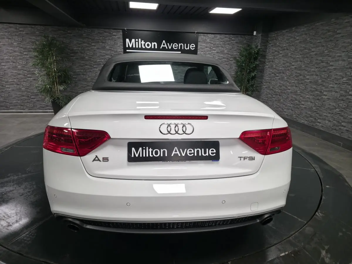 Vue arrière d'une Audi A5 Cabriolet blanche avec capote noire et feux rouges dans un showroom.