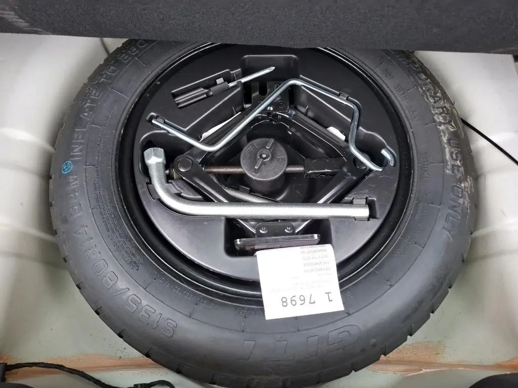 Roue de secours avec outils de changement visibles dans le coffre d'une FIAT 500 blanche Bossa Nova.