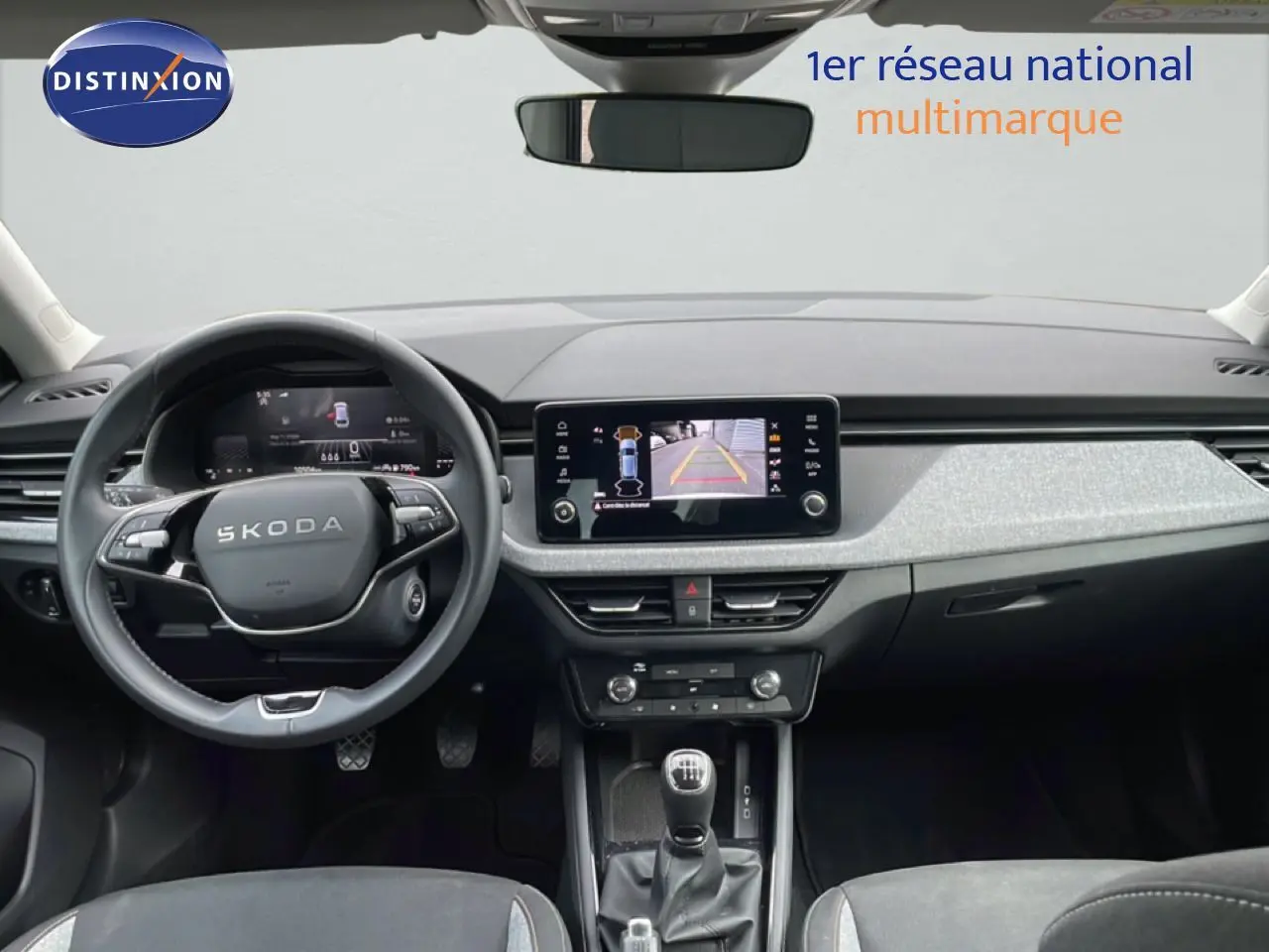 Vue intérieure frontale du tableau de bord gris clair et noir de la Skoda Scala 2025 avec volant cuir et boîte manuelle.