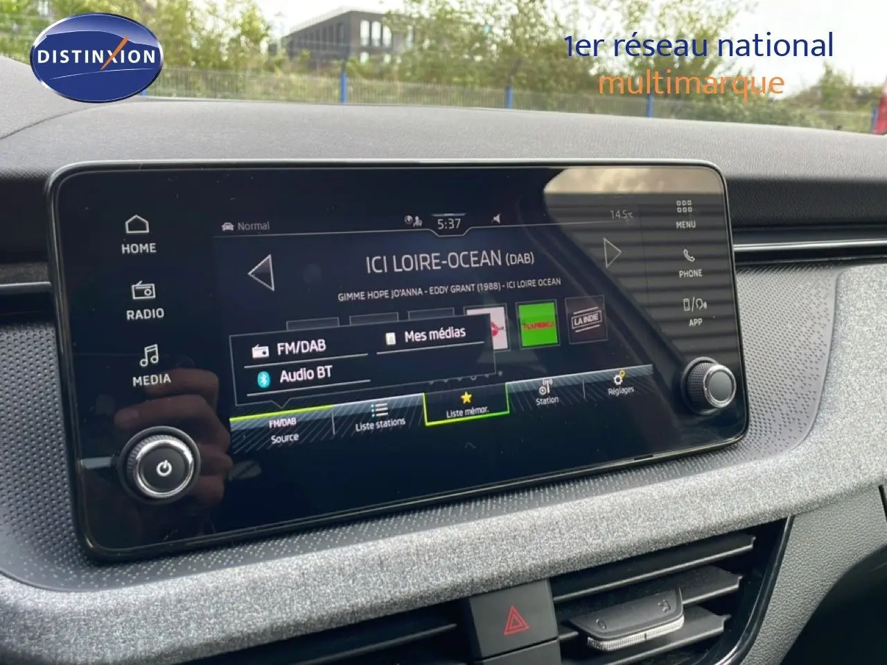 Écran tactile central de la Skoda Scala blanc glacier, affichant la radio FM/DAB avec interface moderne et commandes tactiles.