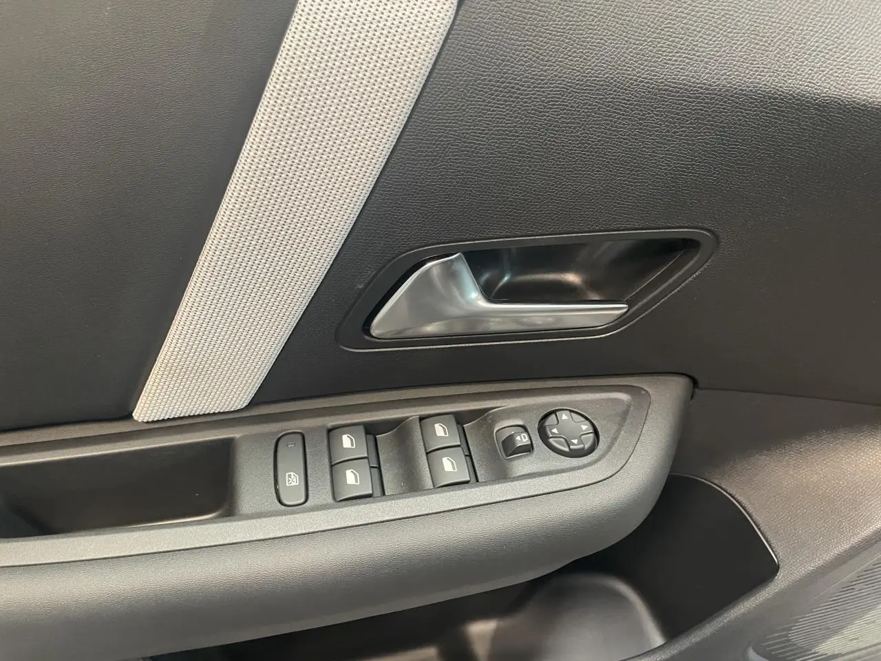Gros plan sur la porte côté gauche de la Citroën C4 gris, avec commandes de vitres et poignée intérieure argentée.