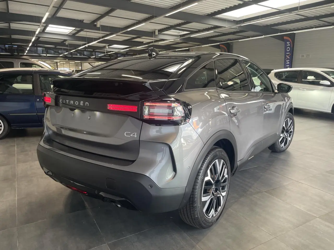 Vue 3/4 arrière droite d'une Citroën C4 grise avec toit noir Perla Nera et jantes alliage 18 pouces en showroom.