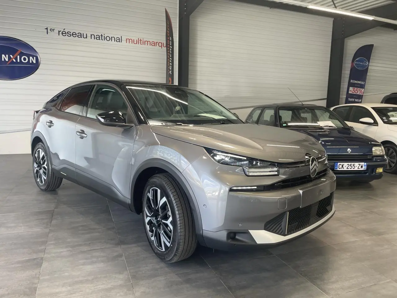 Citroën C4 gris métallisé vue 3/4 avant droit en showroom avec toit bi-ton noir et jantes alliage.