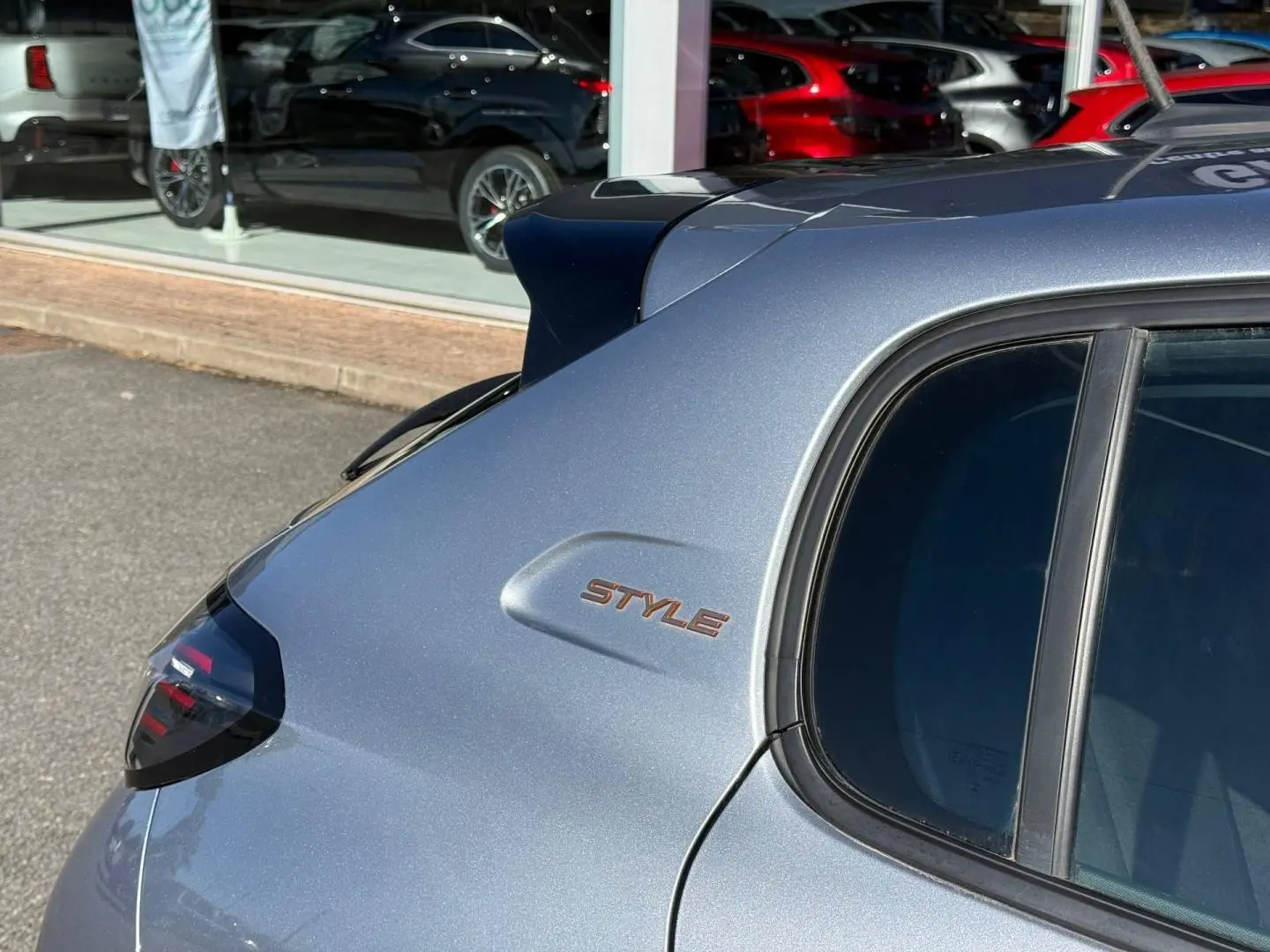 Vue arrière côté gauche d'une Peugeot 208 gris Artense avec logo Style sur la custode et vitres teintées.