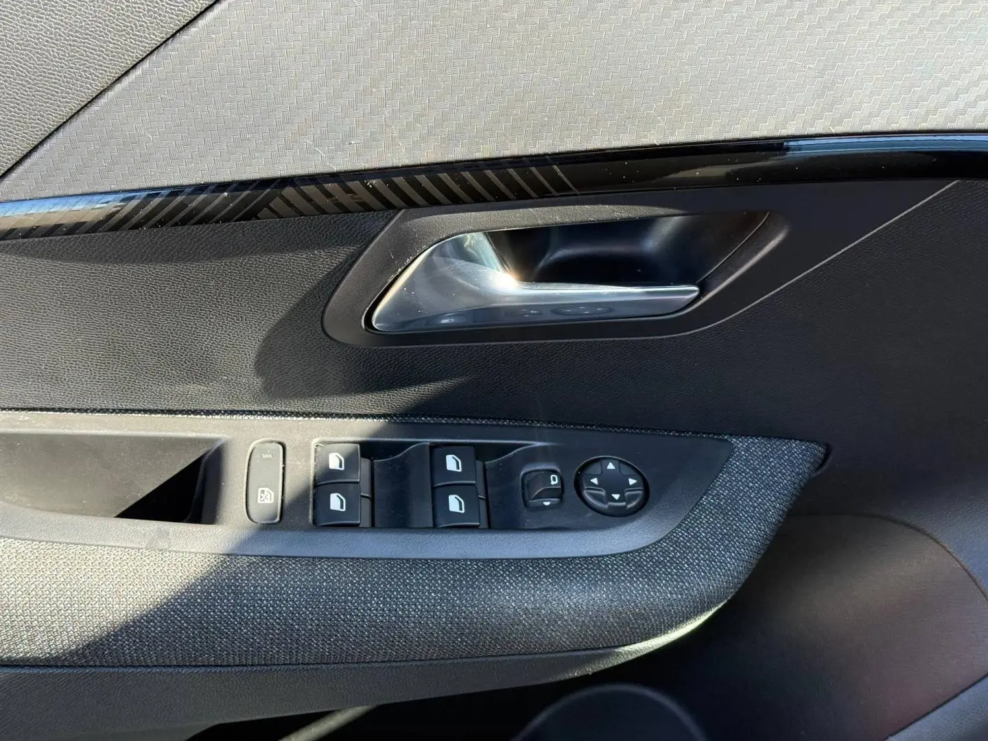 Gros plan sur la porte avant gauche de la Peugeot 208 1.2 Hybrid gris Artense, montrant les commandes des vitres et le bouton de réglage des rétroviseurs.