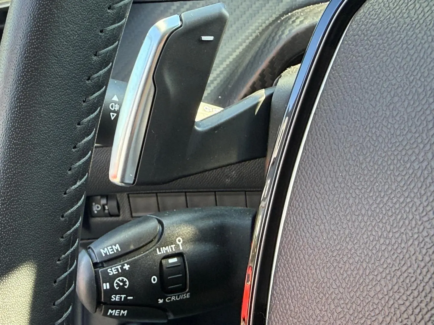 Gros plan sur la commande de régulateur de vitesse à gauche du volant, intérieur tissu gris avec surpiqûres orange.