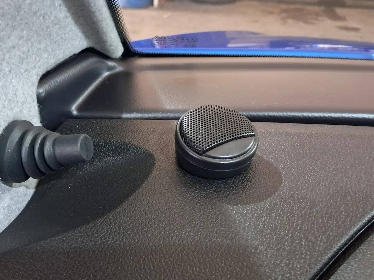 Gros plan sur le haut-parleur intérieur noir dans l'angle supérieur droit du tableau de bord d'une Aixam Ambition bleue.