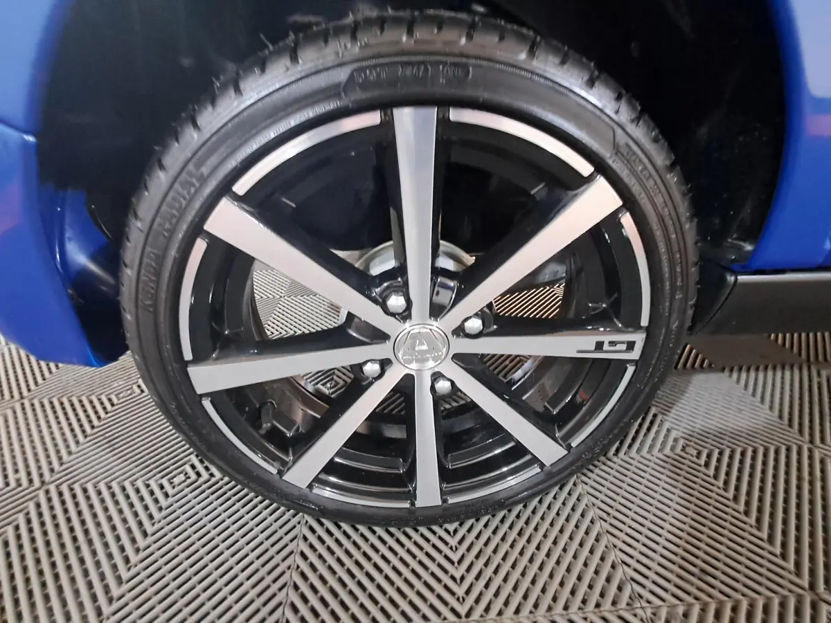 Gros plan sur la jante noire et argentée avec logo Aixam et inscription GT, sur roue avant droite d'une Aixam Ambition bleue.