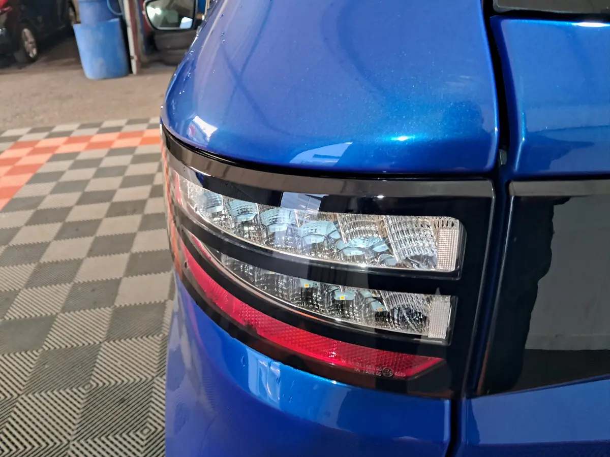 Gros plan sur le feu arrière gauche bleu d'une Aixam Ambition 2025 avec détails lumineux et carrosserie brillante.